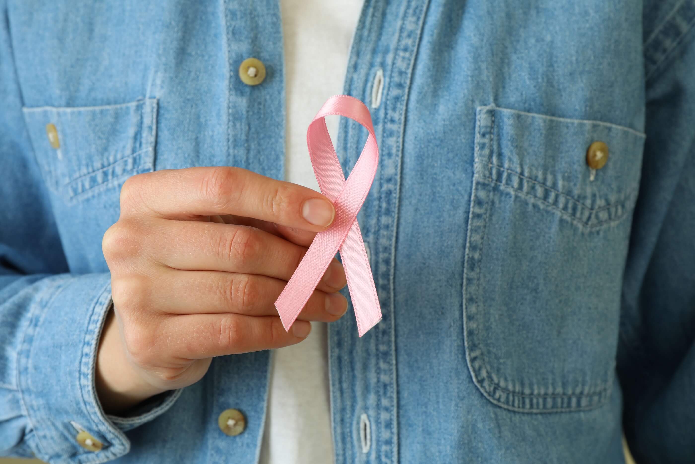 A woman's hands holding a pink breast cancer awareness ribbon in close-up.