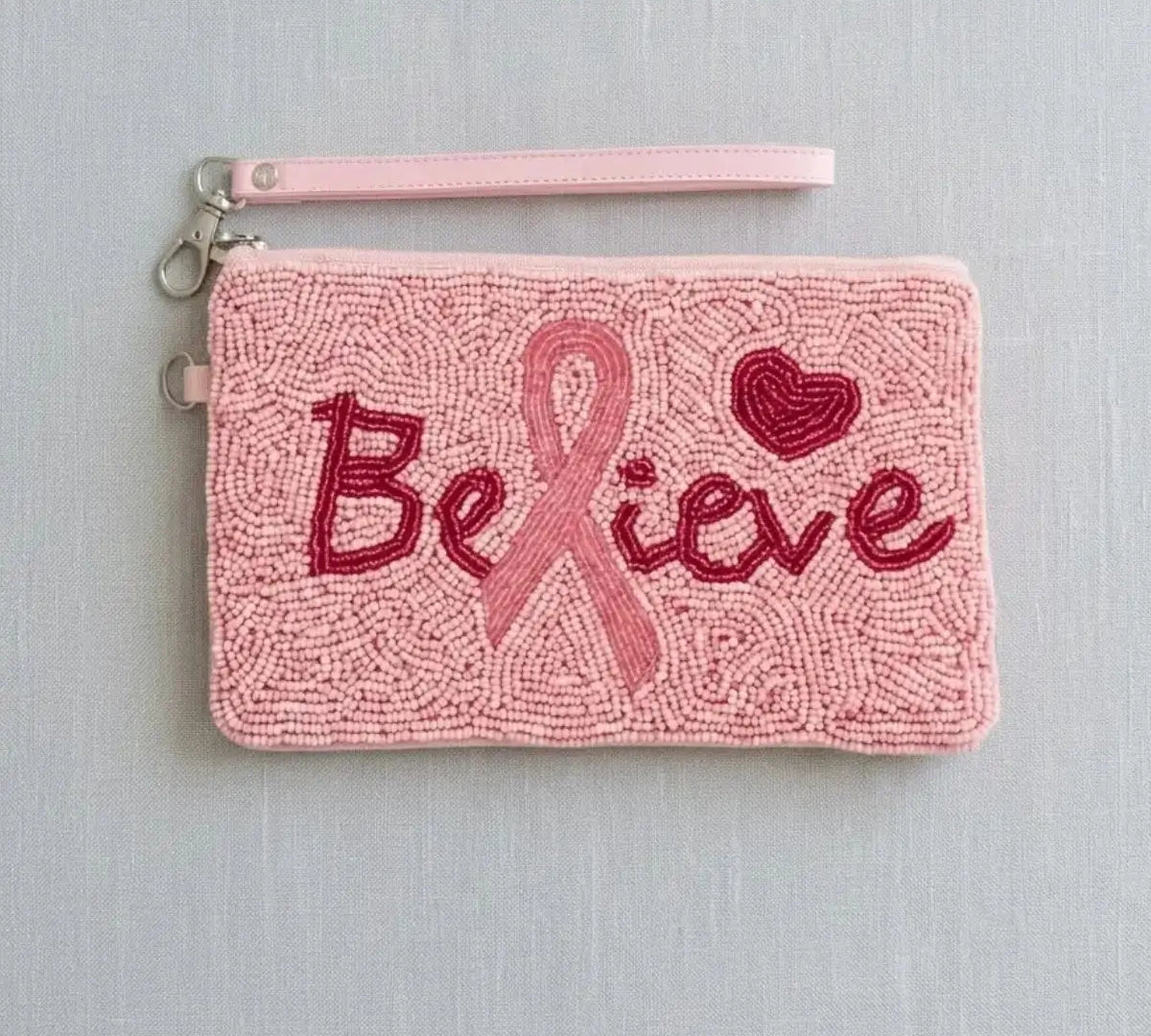 A handmade pink beaded wristlet clutch with a 'Believe' breast cancer awareness ribbon design, featuring red and pink beadwork against a light gray background.