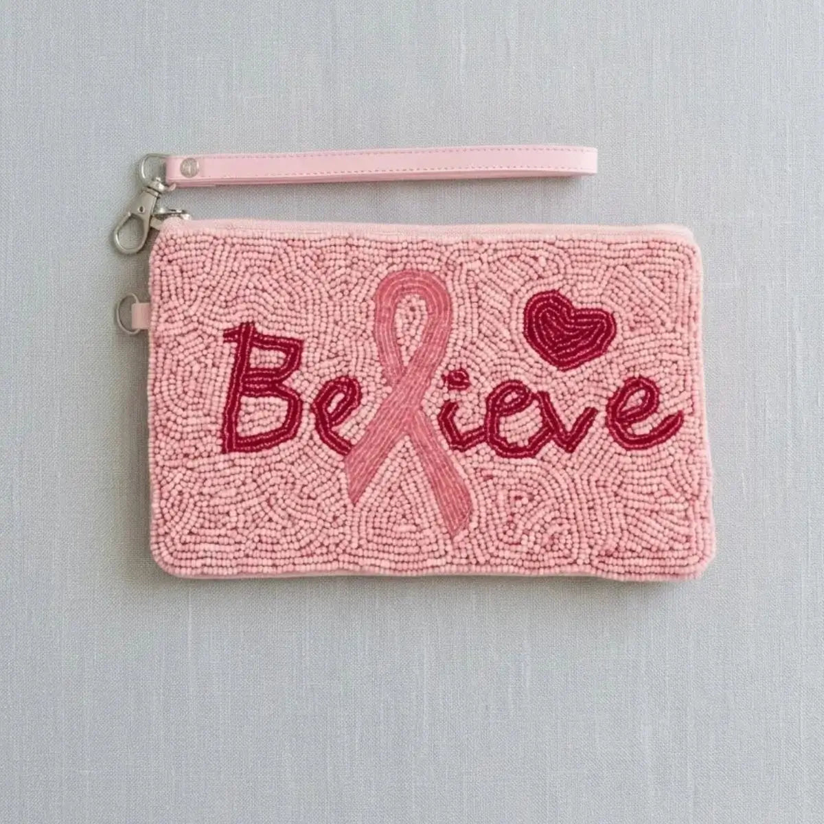 A handmade pink beaded wristlet clutch with a 'Believe' breast cancer awareness ribbon design, featuring red and pink beadwork against a light gray background.