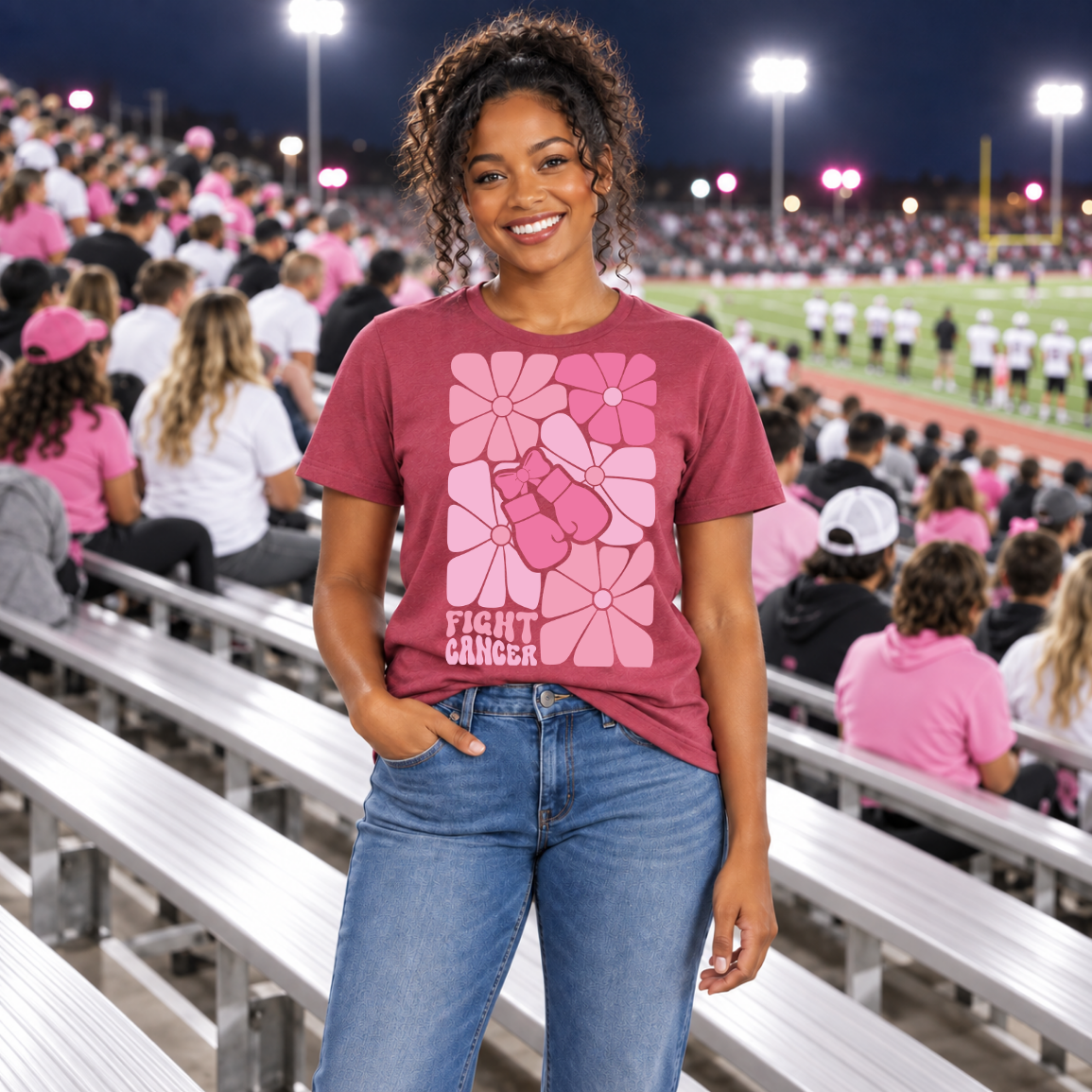 young african american woman standing in a football stadium, wearing a "fight cancer" t-shirt.