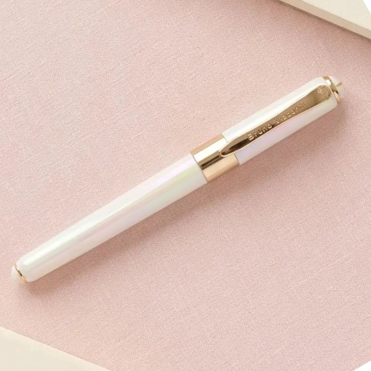 A white iridescent rollerball pen with gold trim and a gold clip, resting diagonally on a textured light pink surface.