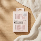 Satin pillowcase in blush pink laid flat beside a folded cloth, a standard size zippered pillowcase that is gentle on hair and skin.