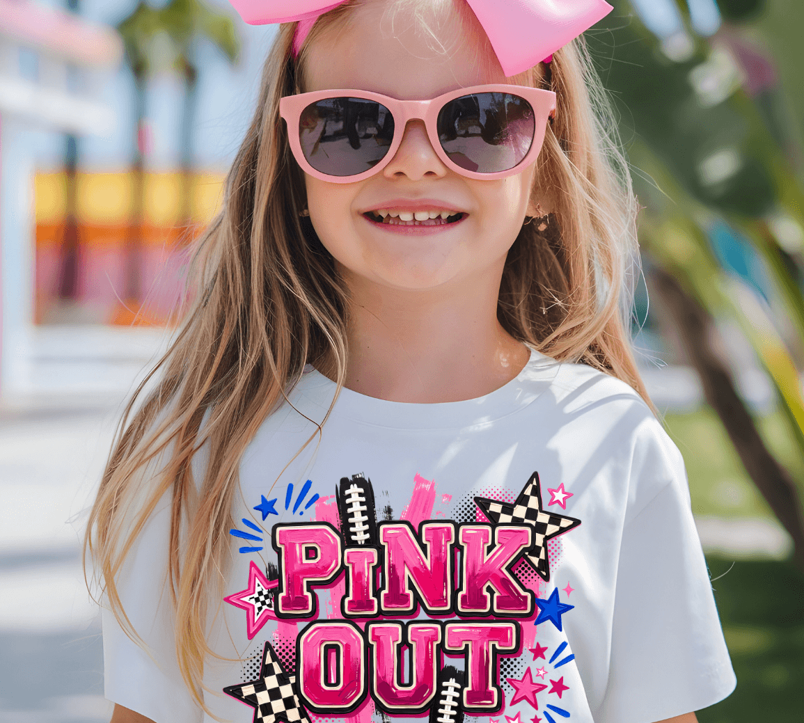A young girl wearing a white graphic t-shirt with a 'PINK OUT' design, pink sunglasses, and a large pink bow in her hair, set against a blurred outdoor background.