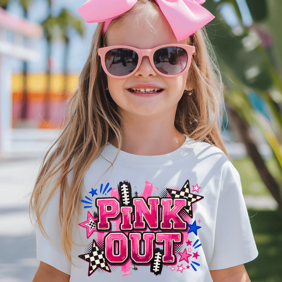 A young girl wearing a white graphic t-shirt with a 'PINK OUT' design, pink sunglasses, and a large pink bow in her hair, set against a blurred outdoor background.