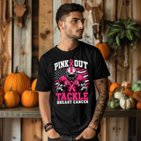 A man wearing a black graphic t-shirt with a pink and white 'Pink Out Tackle Breast Cancer' football player design, posed in front of a rustic wooden wall decorated with pumpkins.