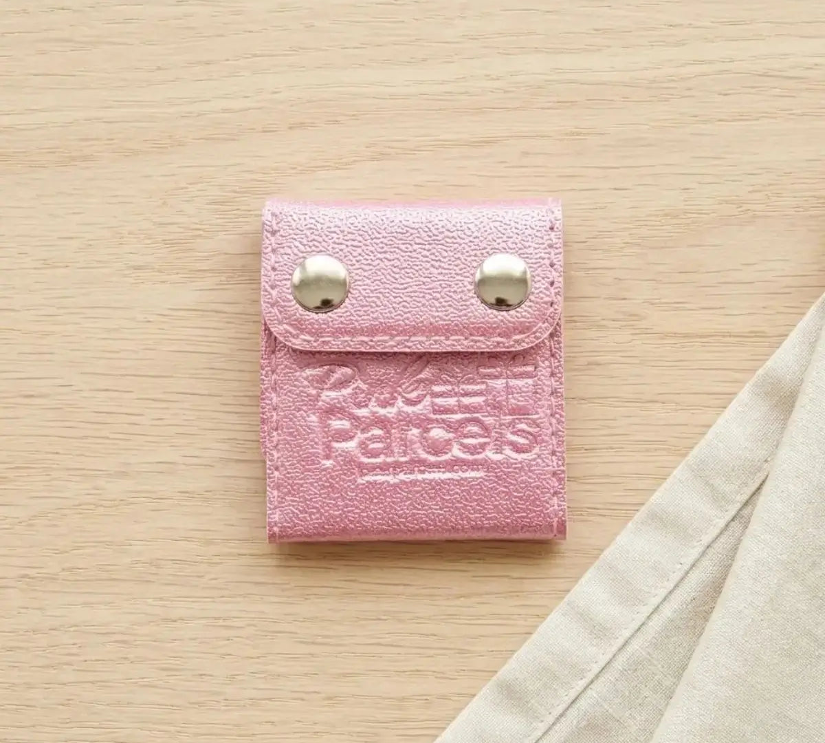 A pink PU leather seat belt adjuster clip stamped with the Pink Parcels logo, used to move a seat belt away from surgery incision sites.