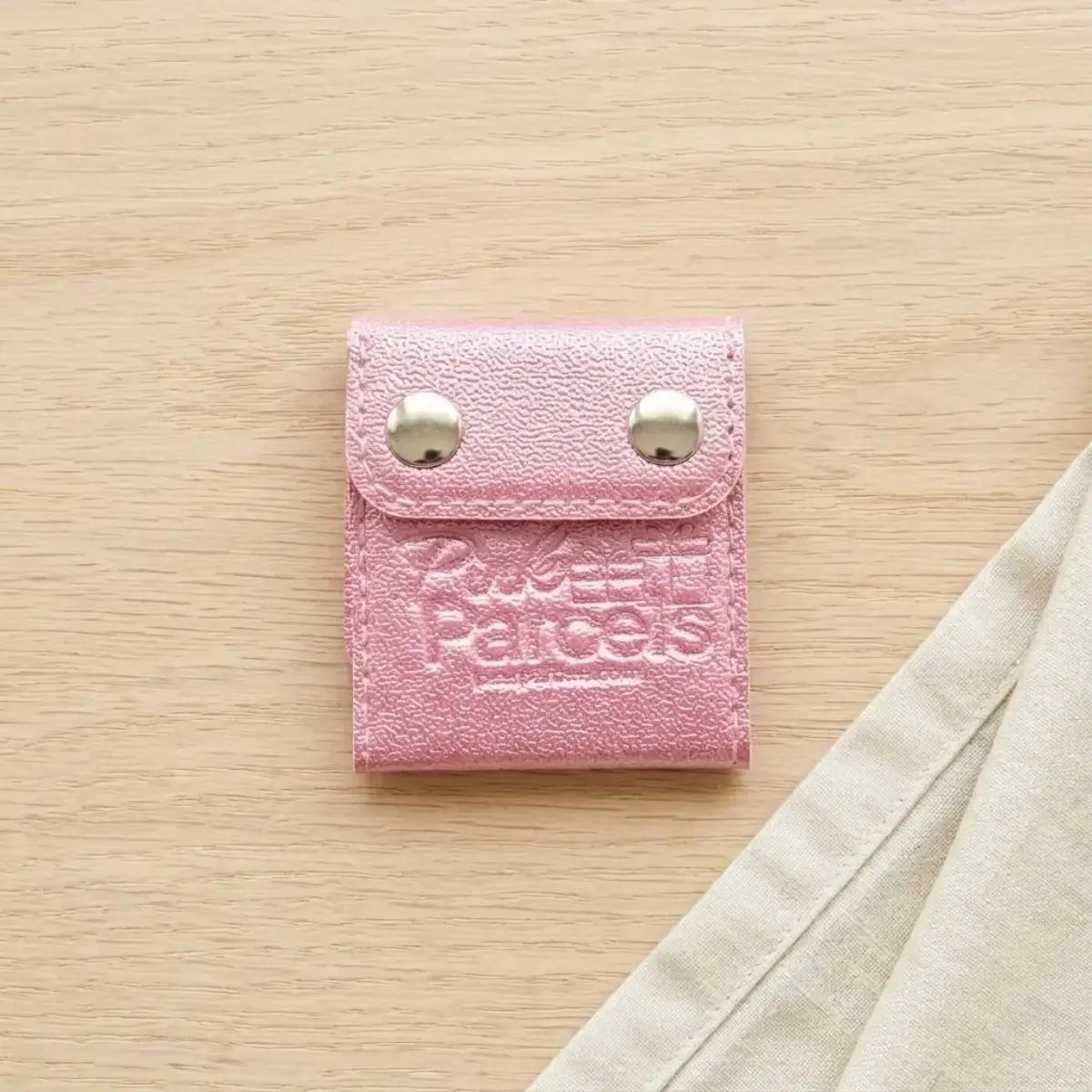 A pink PU leather seat belt adjuster clip stamped with the Pink Parcels logo, used to move a seat belt away from surgery incision sites.