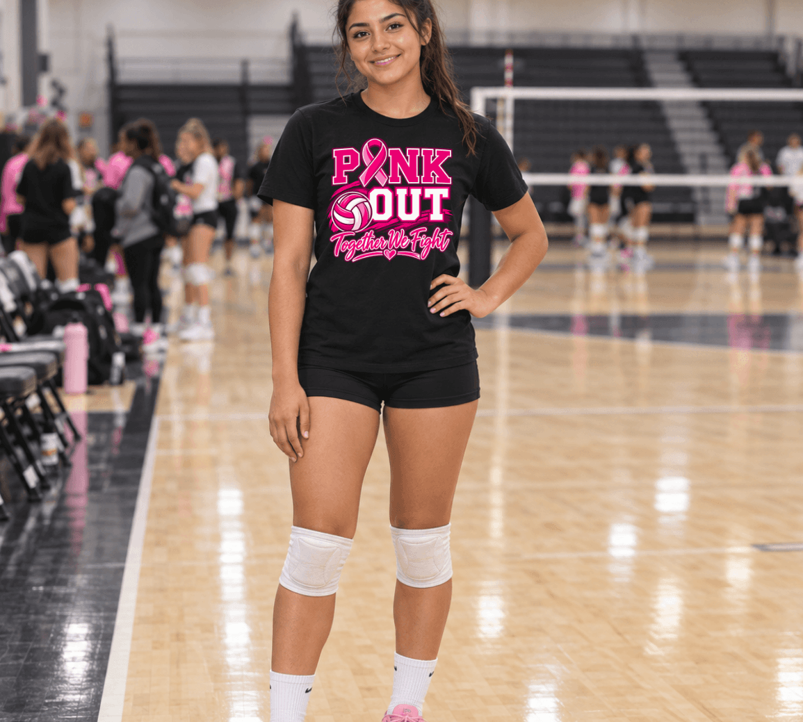 A young woman stands on an indoor volleyball court wearing a black graphic T-shirt that reads 'PINK OUT Together We Fight' in pink and white, paired with black shorts, white knee pads, white socks, and pink sneakers.