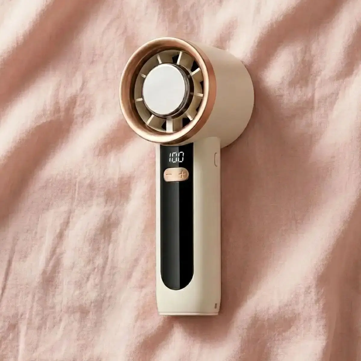 White handheld portable mini fan resting on soft pink fabric from Pink Parcels for breast cancer patients managing hot flashes.